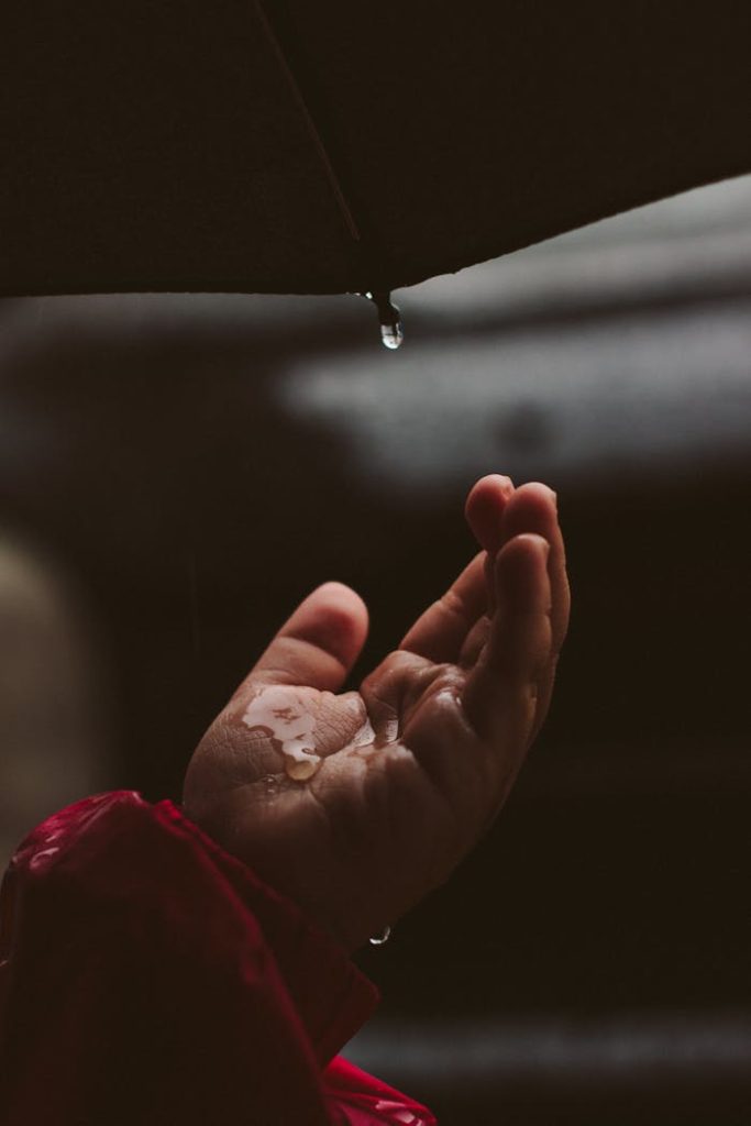 A detailed view of a hand under an umbrella catching falling raindrops.